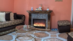 A living room with a fireplace, patterned sofas, and a glass coffee table. - Immaculate 1-bed Apartment in Kingston 14 (Kingston)