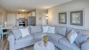 A modern living room with a grey sofa, a round coffee table, and a kitchen in the background. - Bayview Condo right on Lewes Beach (Lewes)
