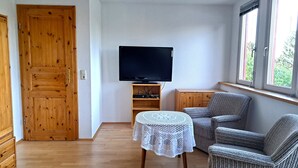 A living room with a wooden door, a television on a stand, a small round table with a white tablecloth, and two grey upholstered chairs. - Geräumige Ferienwohnung "dresdner Stadt-terrasse" für 5 Erw., Kinder Willkommen (Dresden)