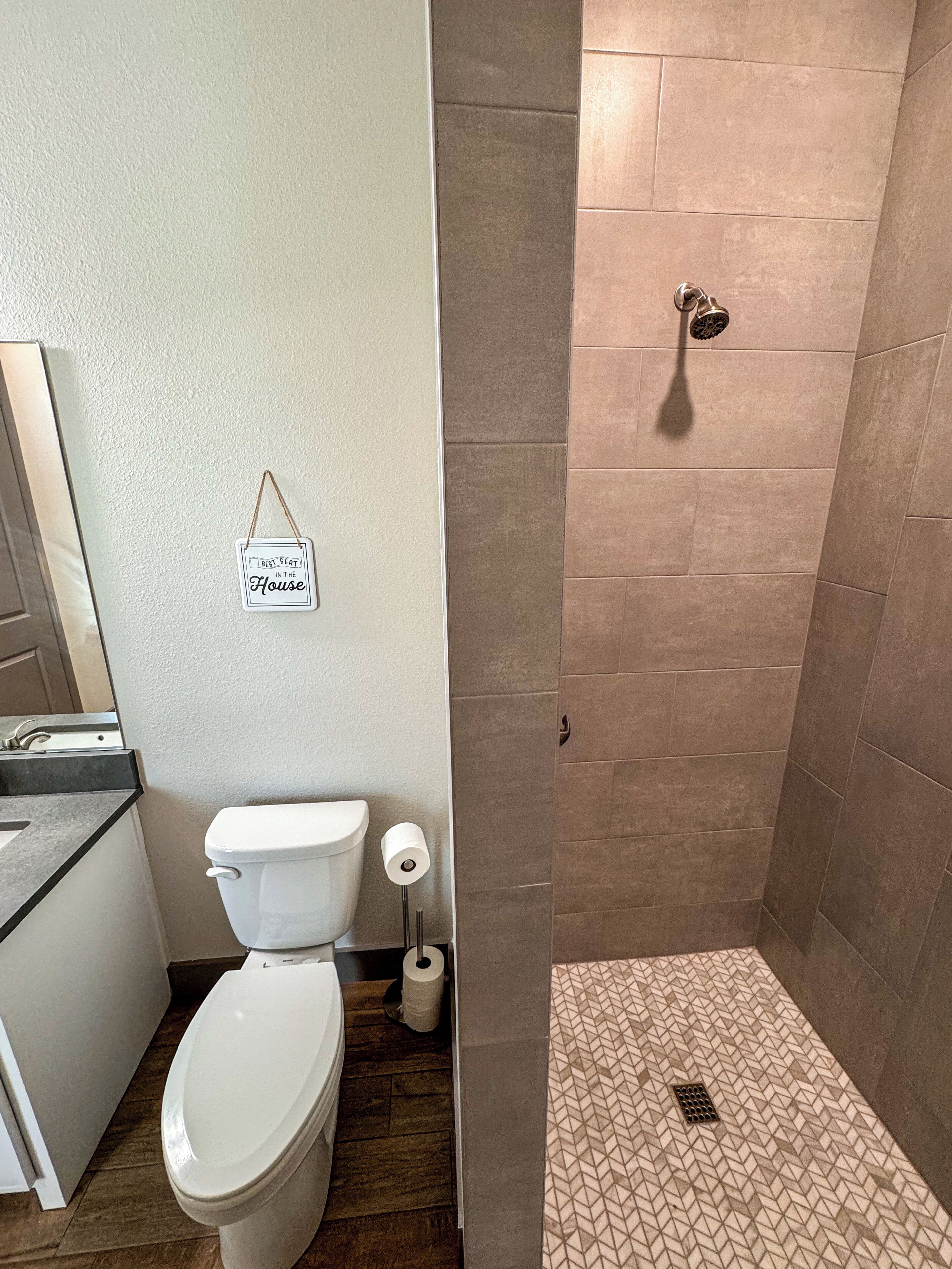 Un baño con inodoro, ducha con pared de azulejos y un cartel colgado en la pared.