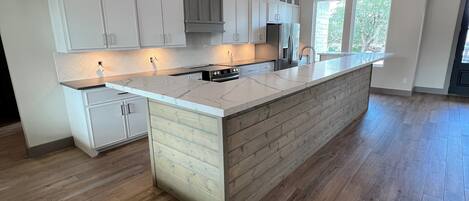 A spacious kitchen with a large island, white cabinetry, and a wooden ceiling.