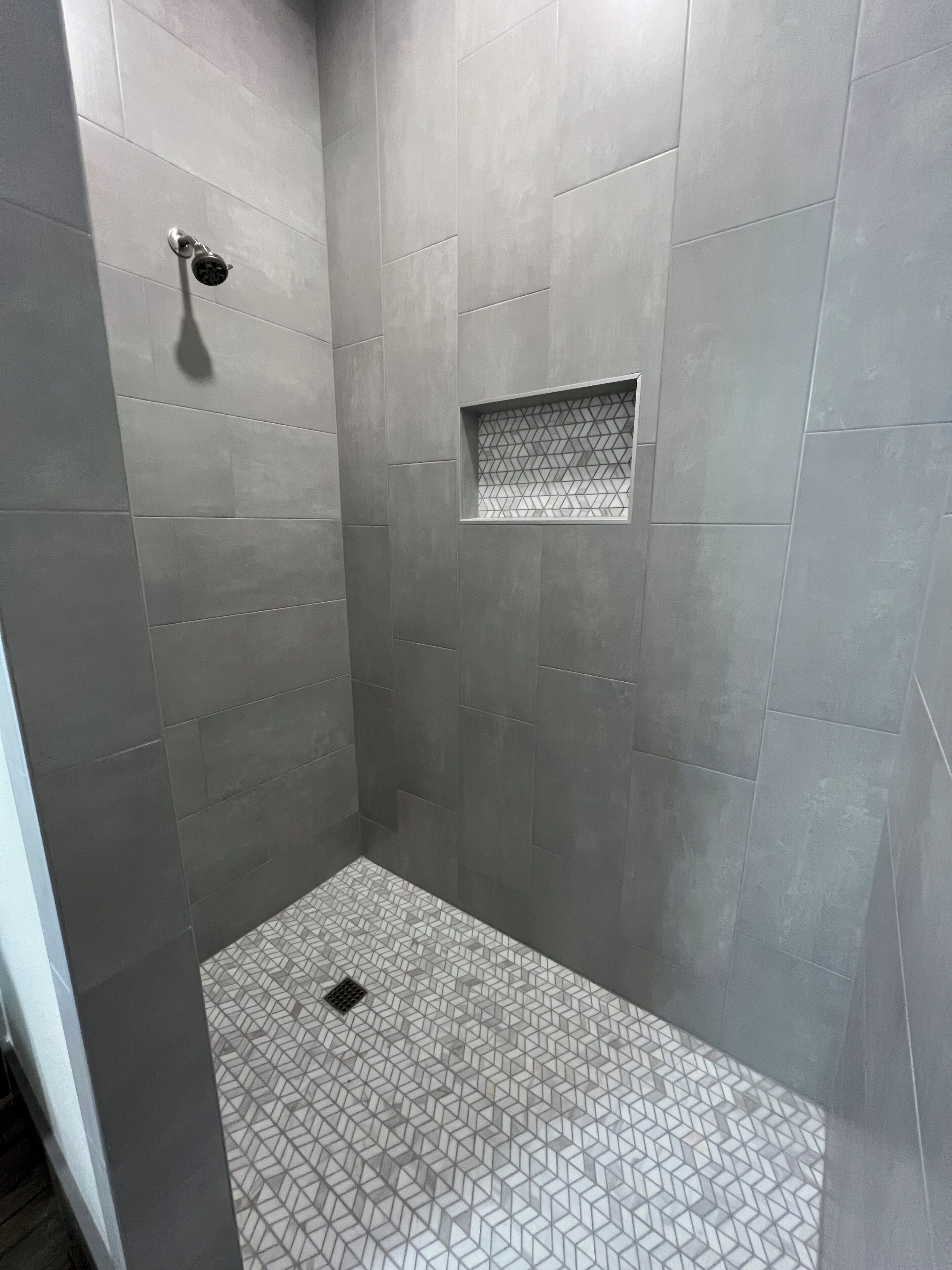 A shower area with grey tiles and a geometric pattern on the floor.