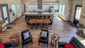 Uma sala de estar ampla com teto alto, uma ilha central com banquetas, uma mesa de jantar e um espaço de estar aconchegante com sofás e cadeiras.