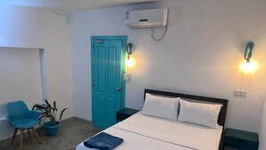 Habitación de hotel con cama, dos mesitas de noche, una silla, una planta en maceta y una puerta.
