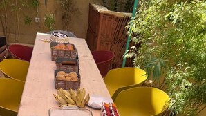 Una larga mesa de madera con diferentes alimentos y utensilios, rodeada de sillas amarillas y rojas.