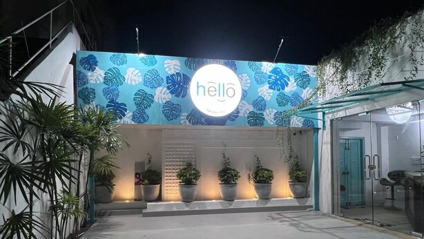 Entrada de un edificio moderno con un cartel que dice 'hello', plantas en macetas y una puerta de cristal.