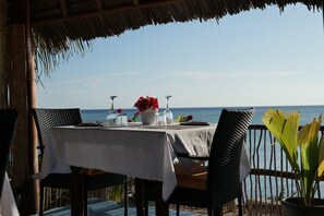 A table set for two with a view of the sea, a thatched roof, and a potted plant. - Lala Land Lodge (Kizimkazi)