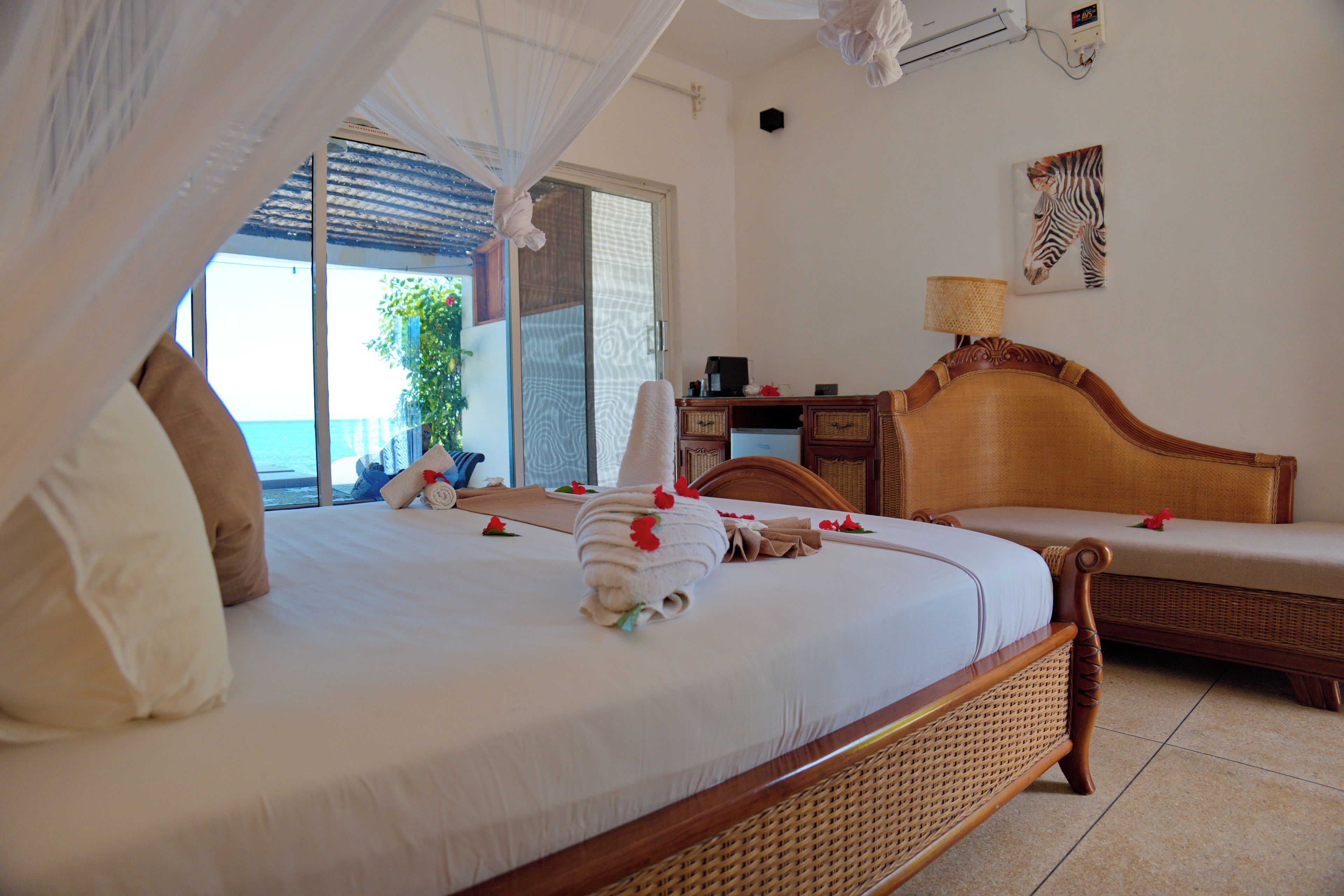 A hotel room with a bed, a desk, a chair, and a view of the sea.
