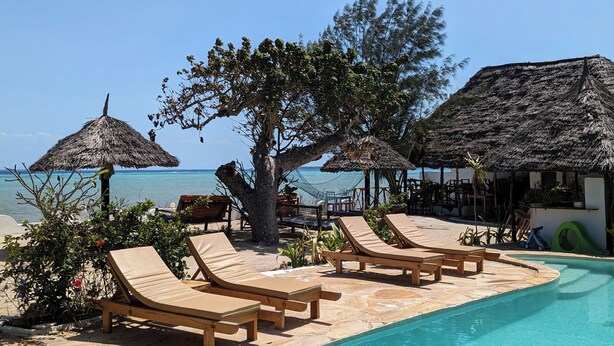 Un espace aménagé au bord de la piscine, avec des chaises longues, une structure à toit de chaume et une vue sur la mer.