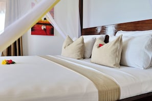 A bed with white linens and beige pillows, a wooden headboard, and a painting on the wall. - Lala Land Lodge (Kizimkazi)
