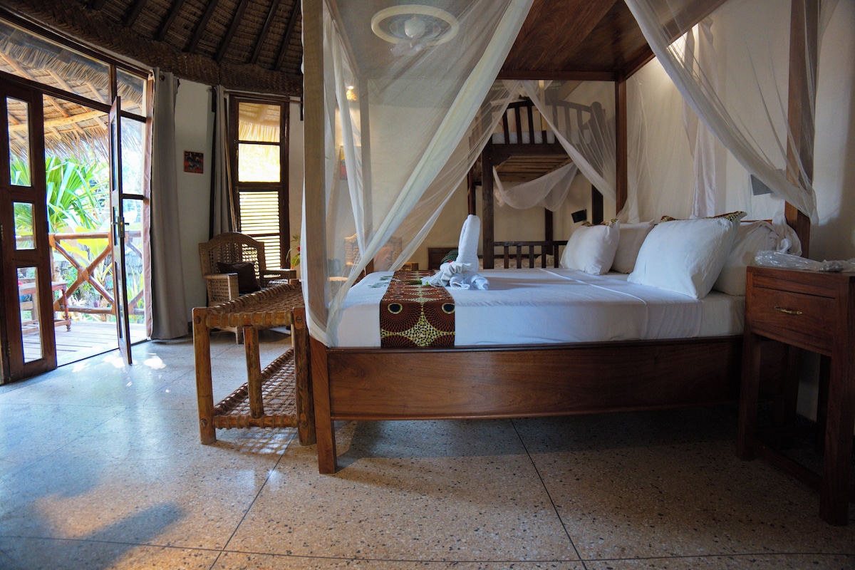 A room with a bed, a wooden nightstand, a wicker chair, and a glass door leading to an outdoor area.
