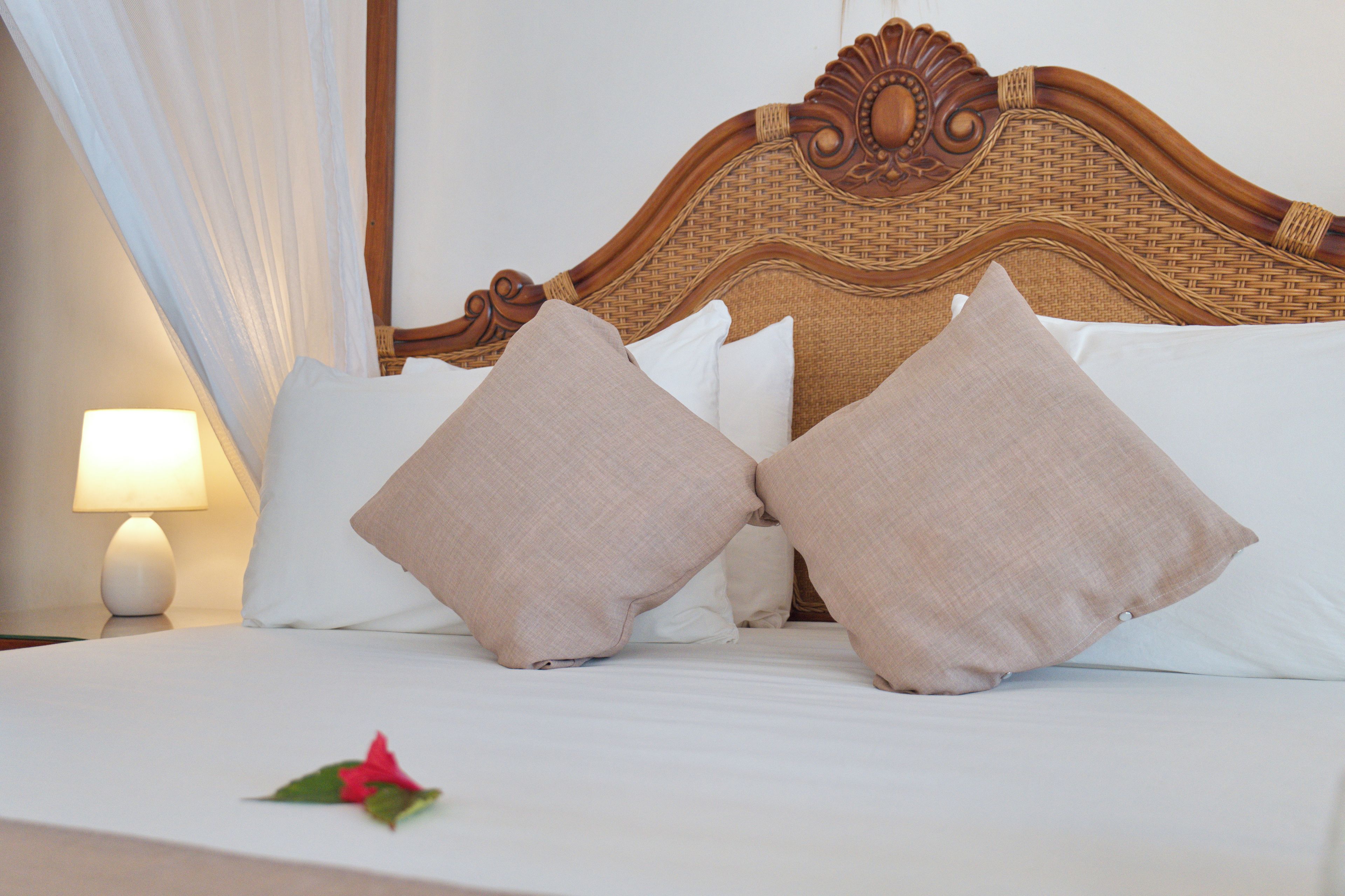 Una cama bien hecha con dos almohadas y una flor sobre el edredón.
