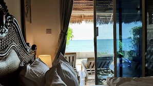 Une chambre à coucher avec un lit, une table de chevet et une vue sur l’océan, visible à travers une porte vitrée.