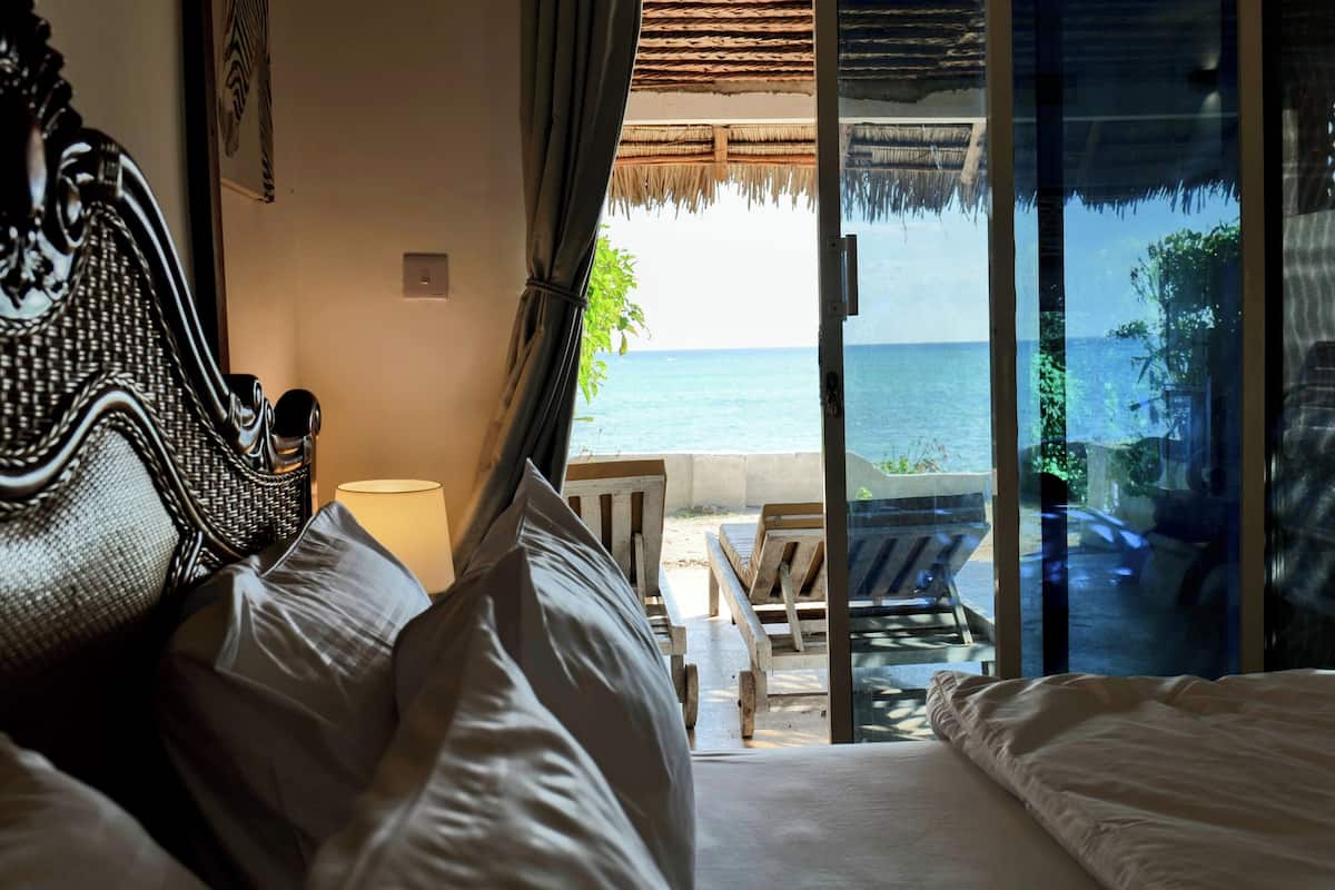 Un dormitorio con cama, mesita de noche y vista al océano a través de un ventanal.