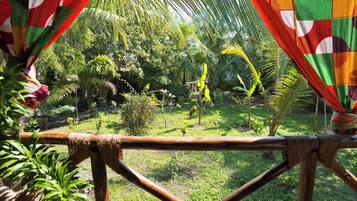 A view from a covered area with a wooden frame, overlooking a garden with various plants and a palm tree.