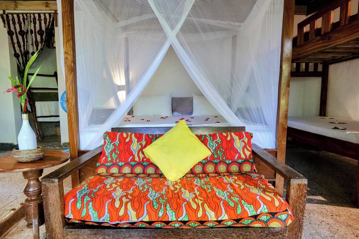 Una cama con dosel, un edredón estampado y vibrante, y una almohada amarilla.