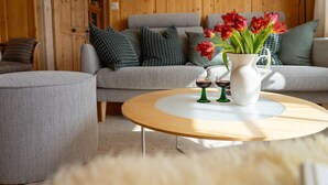 A cozy living room with a grey sofa, a white coffee table, and a vase with red flowers. - Holiday home Nüssli for 6 people with fantastic mountain views (Wildhaus)