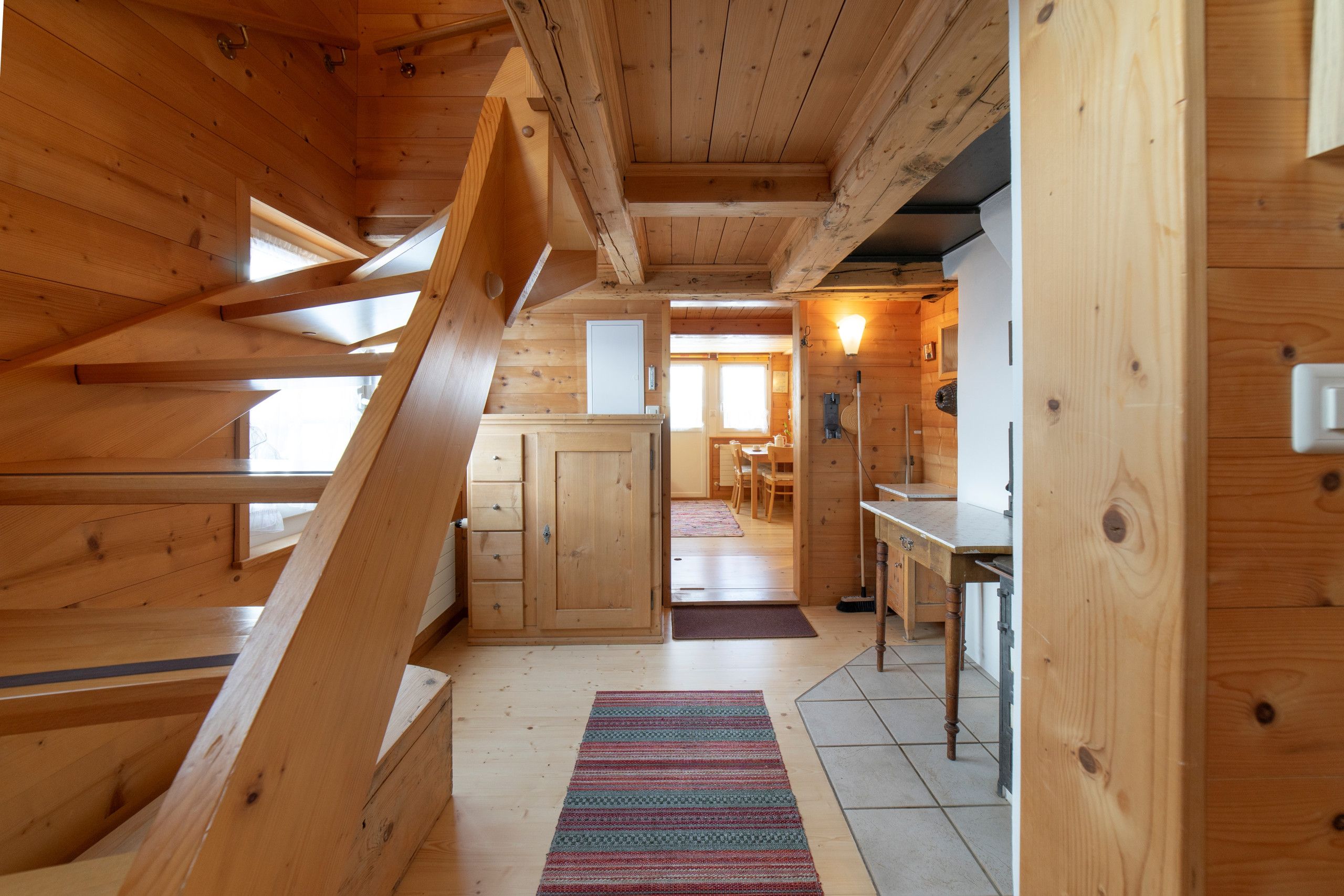 A wooden interior with a staircase, a kitchen area, and a dining space.