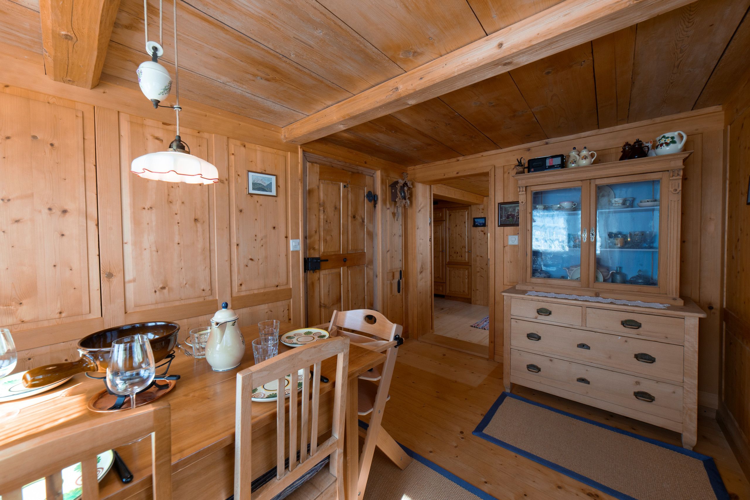 A wooden interior with a dining table, chairs, a cabinet with glass doors, and a ceiling light fixture.
