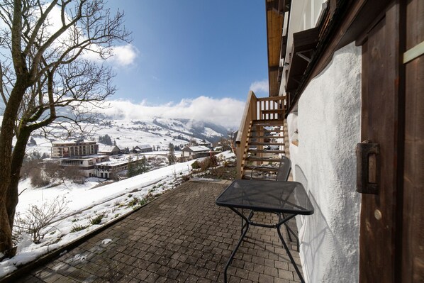 A snow-covered outdoor area with a wooden staircase leading to a building, a paved walkway, and a view of a snow-covered village in the distance. - Holiday home Nüssli for 6 people with fantastic mountain views (Wildhaus)