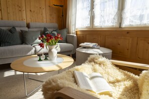 A cozy living room with a sofa, a coffee table, a rug, and a window with curtains. - Holiday home Nüssli for 6 people with fantastic mountain views (Wildhaus)