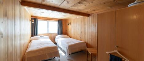A room with two beds, a wooden wardrobe, a small table, and a window with curtains.