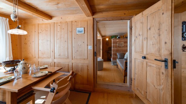 A wooden interior with a dining table, chairs, and a kitchen area visible through an open door. - Holiday home Nüssli for 6 people with fantastic mountain views (Wildhaus)