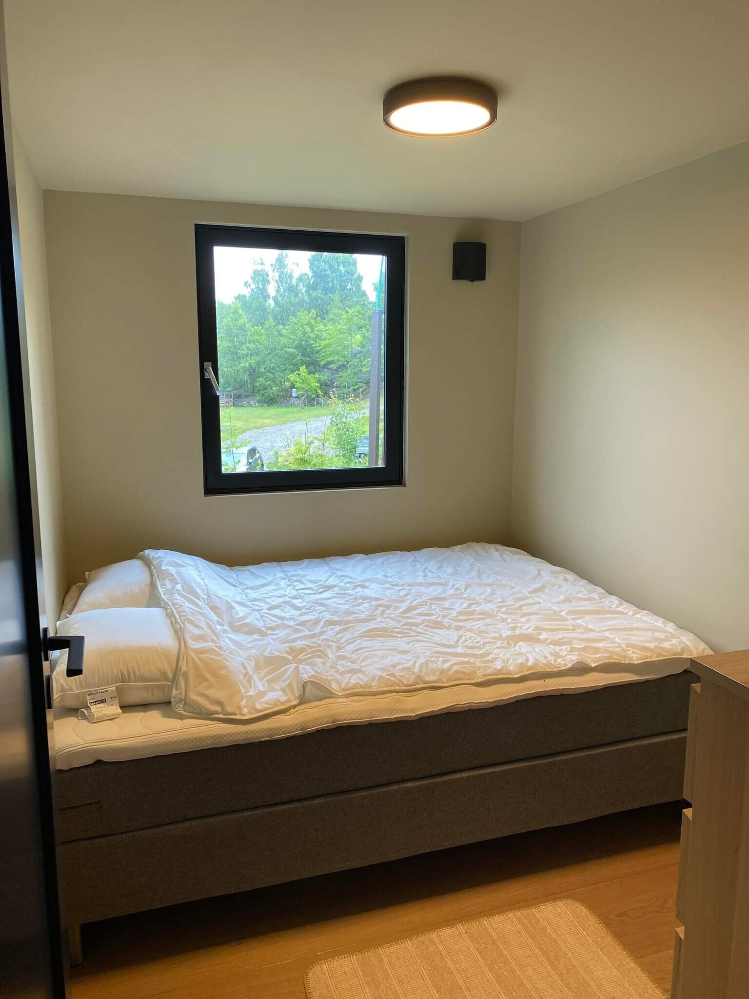 Een slaapkamer met een bed, een raam en een plafondlamp.