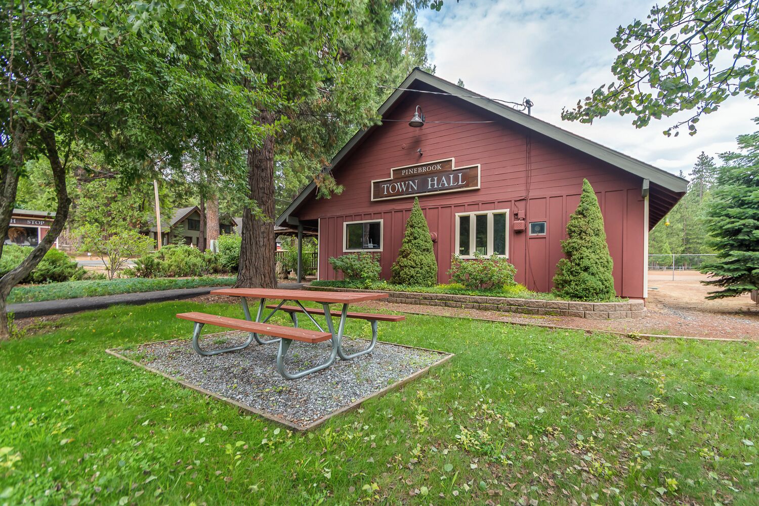 A red building labeled "Pinebrook Town Hall" with a picnic table in front.