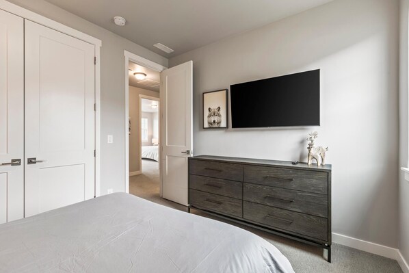 A bedroom with a bed, a dresser, a television, and a hallway leading to another room.
