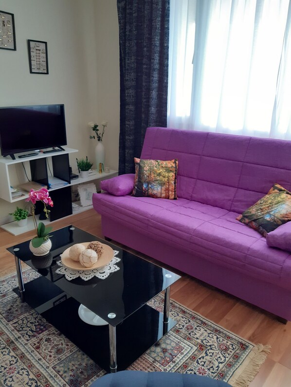 A living room with a purple sofa, a black coffee table with decorative items, a flat-screen TV on a white stand, and a patterned rug. - Ocean orchidea appartment with breathtaking view just at the ocean (Puerto de la Cruz)