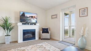 Una sala de estar con chimenea, televisor, una silla y un ventanal grande.