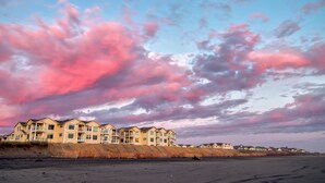 Ein Strandhotel mit mehreren Balkonen und einem Sandstrand im Vordergrund.