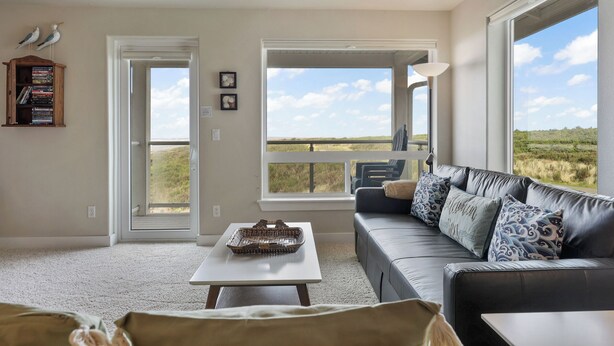 A living room with a large window, a leather sofa, a coffee table, and a bookshelf.