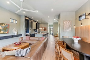 A modern living room with a leather sofa, a dining table, and a kitchen in the background. - 5BR NOLA Home | Heated Pool & Rooftop Deck (New Orleans)