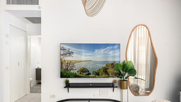A modern living room with a large flat-screen TV, a round mirror, and a potted plant. - Comfortable apartment with Balcony by HolyGuest (Tel Aviv)