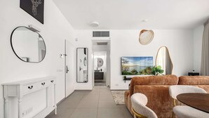 A modern living room with a white console table, a round mirror, a television, and a brown sofa set. - Comfortable apartment with Balcony by HolyGuest (Tel Aviv)