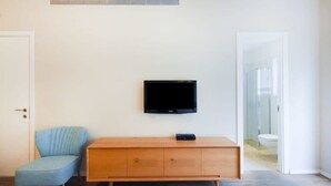 Huoneessa on puinen kaappi, sininen tuoli ja seinälle asennettu televisio.