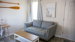 Una habitación con un sofá gris, una mesa de centro de madera, un escritorio blanco con una silla y dos palas de madera en la pared.