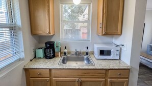 Una cocina con armarios de madera, encimera de granito, un lavamanos, cafetera, tostadora y microondas.