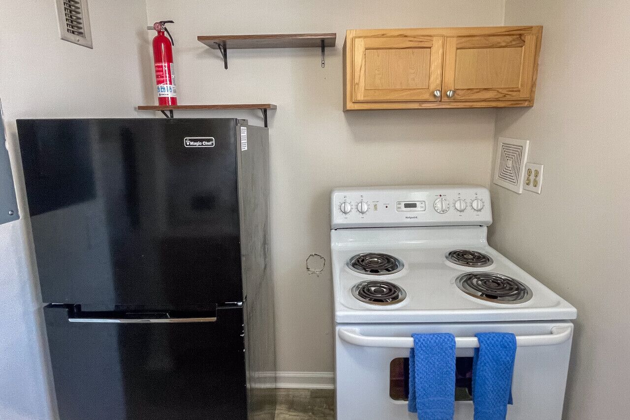 Cocina compacta con un refrigerador negro, estufa blanca y armarios de madera.