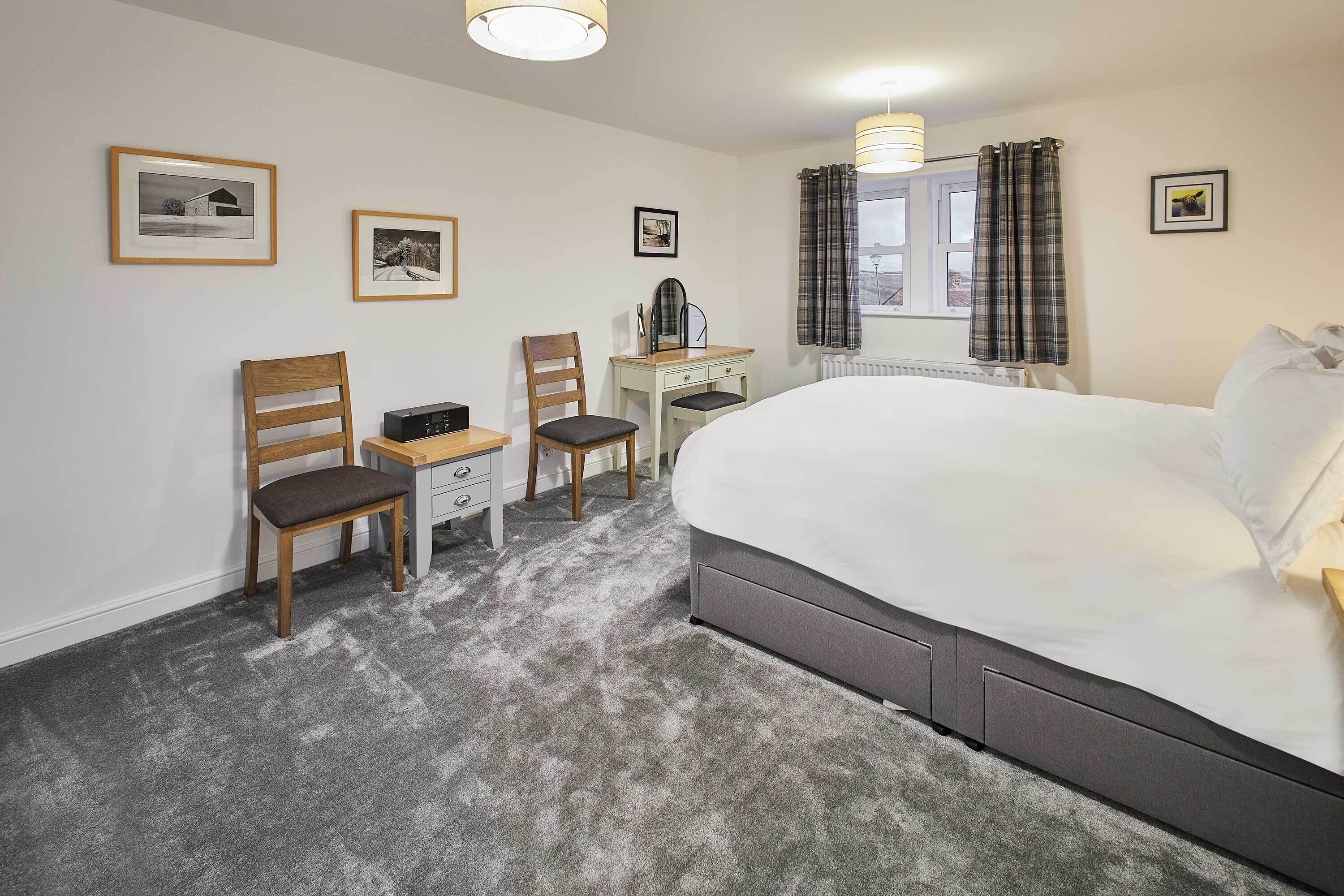Ett hotellrum med en stor säng, två trästolar, ett skrivbord och ett fönster med gardiner.
