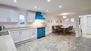Una cocina moderna con armarios blancos, una campana extractora azul y un comedor con mesa y sillas.