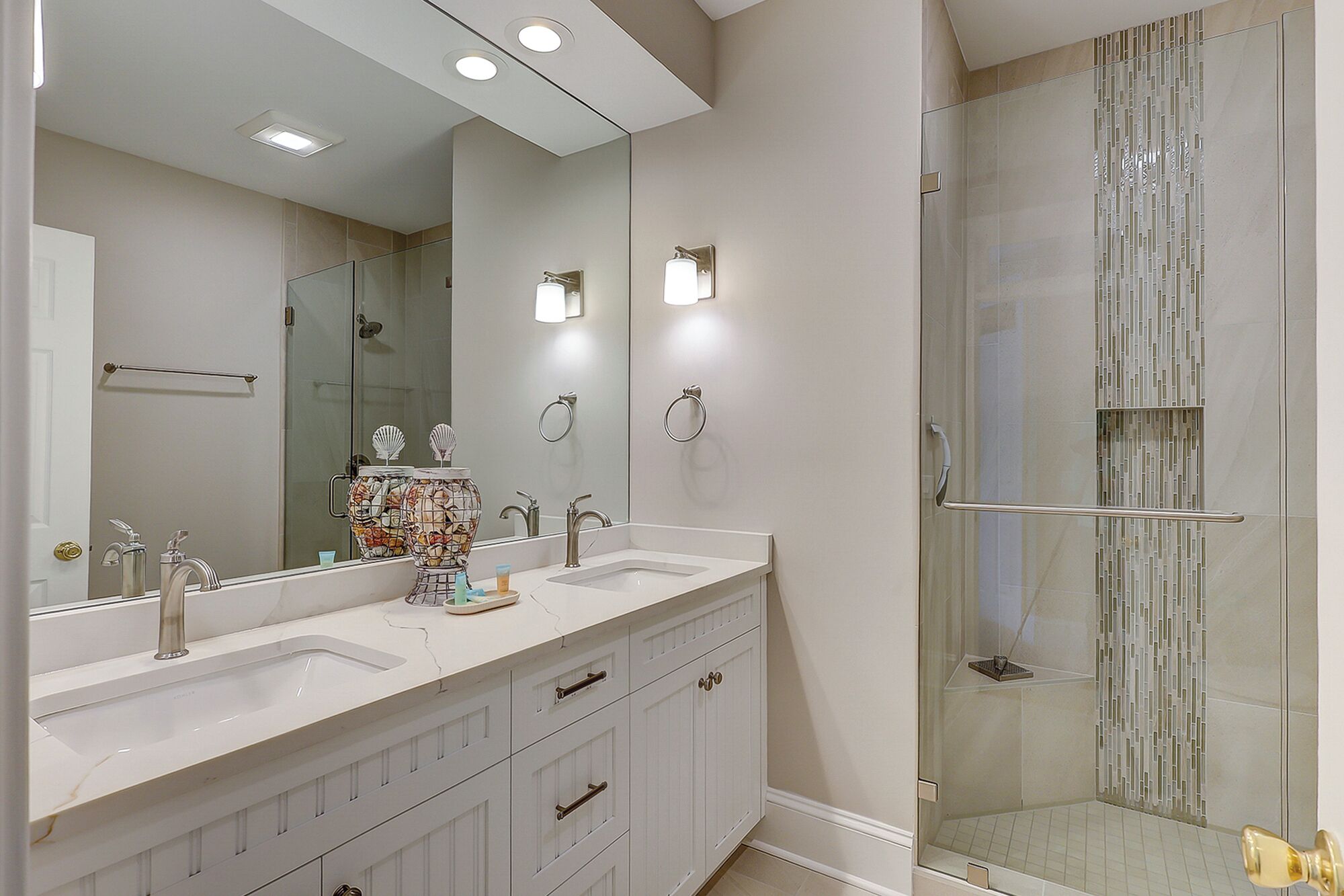 A bathroom with two sinks, a large mirror, a glass shower enclosure, and a toilet with a decorative cover.