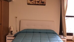 Une chambre avec un plafond en bois, un lit recouvert d’une couette bleue, une table de chevet avec une lampe et un tableau accroché au mur.