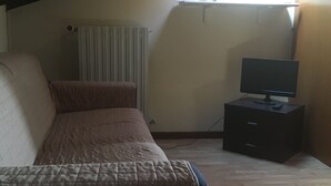 Une chambre à coucher avec un lit, un téléviseur posé sur une commode et un radiateur.