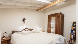 A bedroom with a large bed, wooden headboard, a wardrobe, bedside lamps, and a bookshelf. - Seafront Evi's Hideaway - Petalidi Cozy Nest (Petalidi)