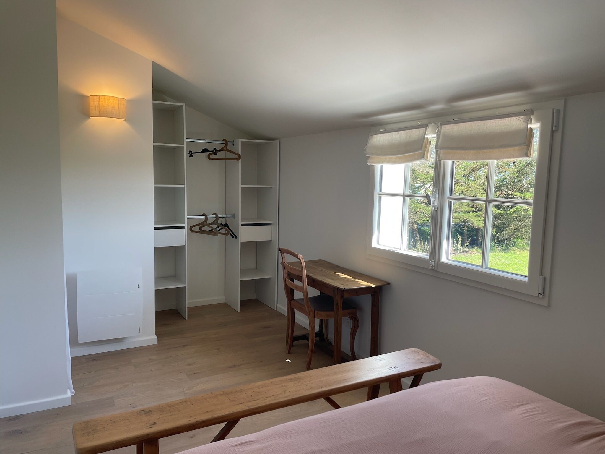 Ein Zimmer mit Schreibtisch aus Holz, einem Sessel, einer Bank und einem großen Kleiderschrank mit Ablagefläche.