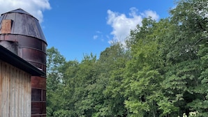 A rustic barn with a cylindrical silo, surrounded by a well-maintained lawn and dense trees. - RV lot Hook Up, 5 minutes off I 80. Peacefully hidden behind our vintage barn.  (Loganton)