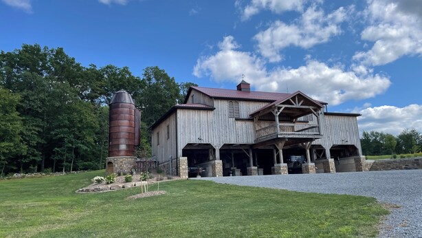 A rustic barn-style building with a large silo, a covered porch, and a well-maintained lawn. - RV lot Hook Up, 5 minutes off I 80. Peacefully hidden behind our vintage barn.  (Loganton)